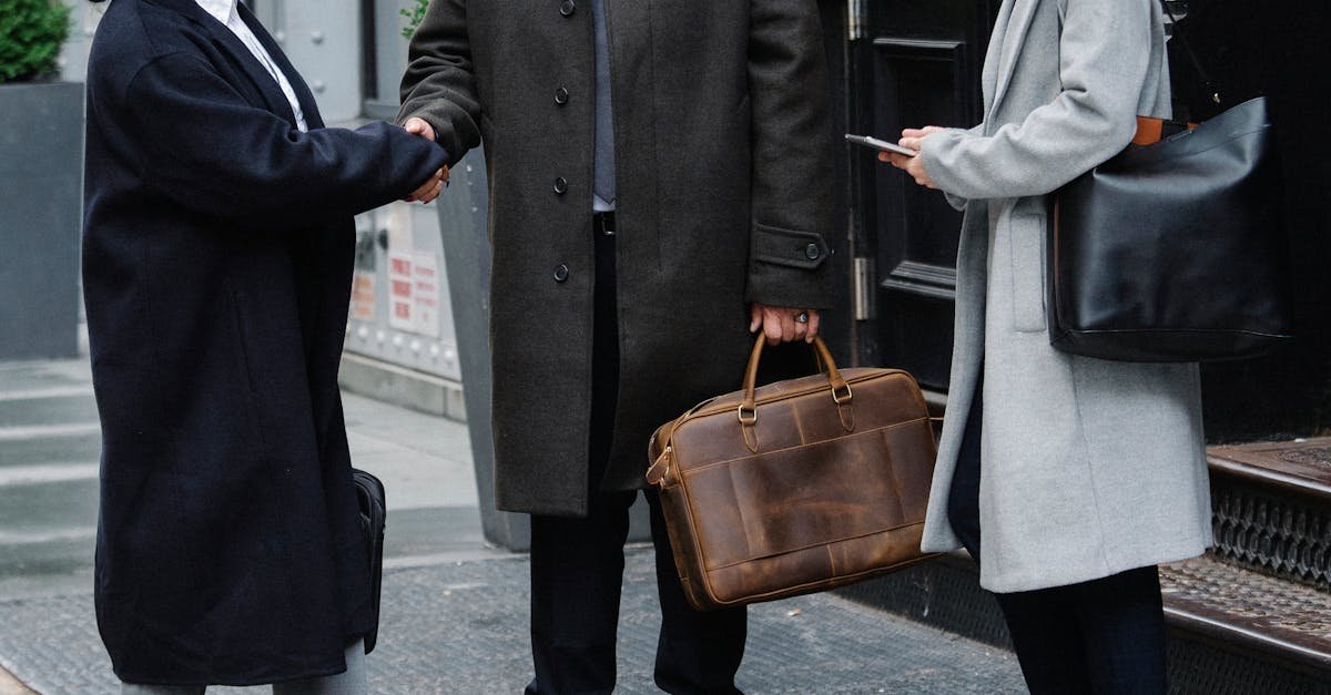 Crop anonymous trendy businessman and businesswomen in elegant outerwear shaking hands on street